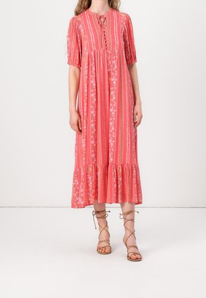 Femme portant une robe midi corail rose avec des rayures florales verticales, des manches bouffantes, des boutons sur le devant et des sandales lacées couleur beige.
