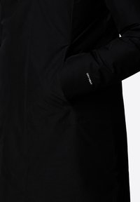 Zwarte waterdichte jas met een gladde textuur, voorzien van een zijvak en een manchetlabel met de tekst "DRY VENT." Eenvoudig ontwerp, functionele stijl.