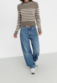 Brun og creme-stribet cropped sweater parret med løse blå denimjeans og hvide sneakers. Blød tekstur og afslappet pasform.