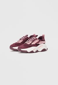 Baskets de sport en bordeaux foncé et rose, avec un matériau en maille et en daim, une semelle blanche épaisse et un design à lacets avec des accents de logo.