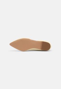 Semelle d'une chaussure plate beige clair à bout pointu avec une semelle lisse couleur fauve et un petit talon, présentée sur fond blanc.