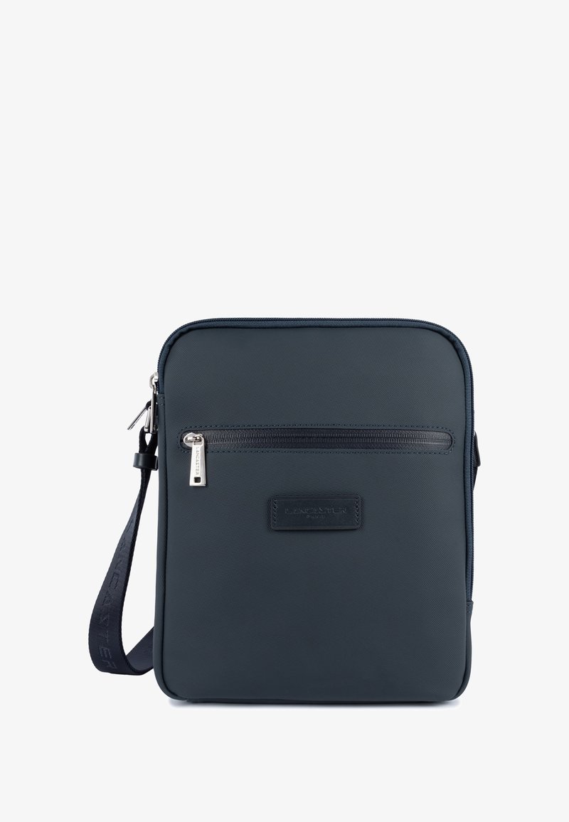 Borsa a tracolla sintetica di colore blu scuro con una tasca frontale con zip, design piatto, dettagli in pelle e tracolla regolabile. Il tirante della zip presenta il marchio.