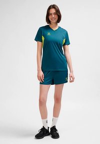 Sportoutfit i blågrönt med gula detaljer; kortärmad tröja och matchande shorts, tillverkade av lätt material, med v-ringad design.