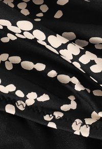 Tela negra con un patrón texturizado de formas irregulares en beige. La costura visible a lo largo del borde añade detalle al diseño.