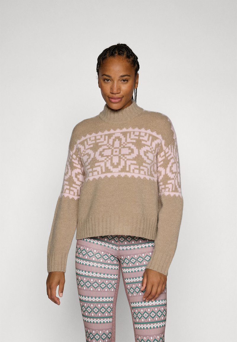 Suéter de punto beige con un yugo de patrón rosa, con un cuello alto y puños acanalados. Combinado con mallas estampadas en tonos rosa y azul.