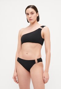 Juodas vieno peties bikini viršus su rifliuota tekstūra, reguliuojama petneša ir atitinkamas žemas bikini dugnas, turintis šoninės aparatūros akcentą.