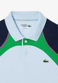 Polo shirt azzurro chiaro con dettagli in navy, verde e rosa. Presenta un design testurizzato, tre bottoni e un logo Lacoste sul petto.