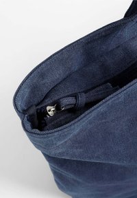 Sac en tissu bleu marine avec une fermeture éclair, présentant une surface texturée et des détails de couture minimalistes. L'intérieur semble sombre et spacieux.