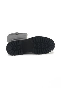 Botte en caoutchouc noire avec une semelle texturée, dotée de profondes rainures pour une meilleure adhérence et d'une sangle sur le dessus avec un détail de boucle en argent.