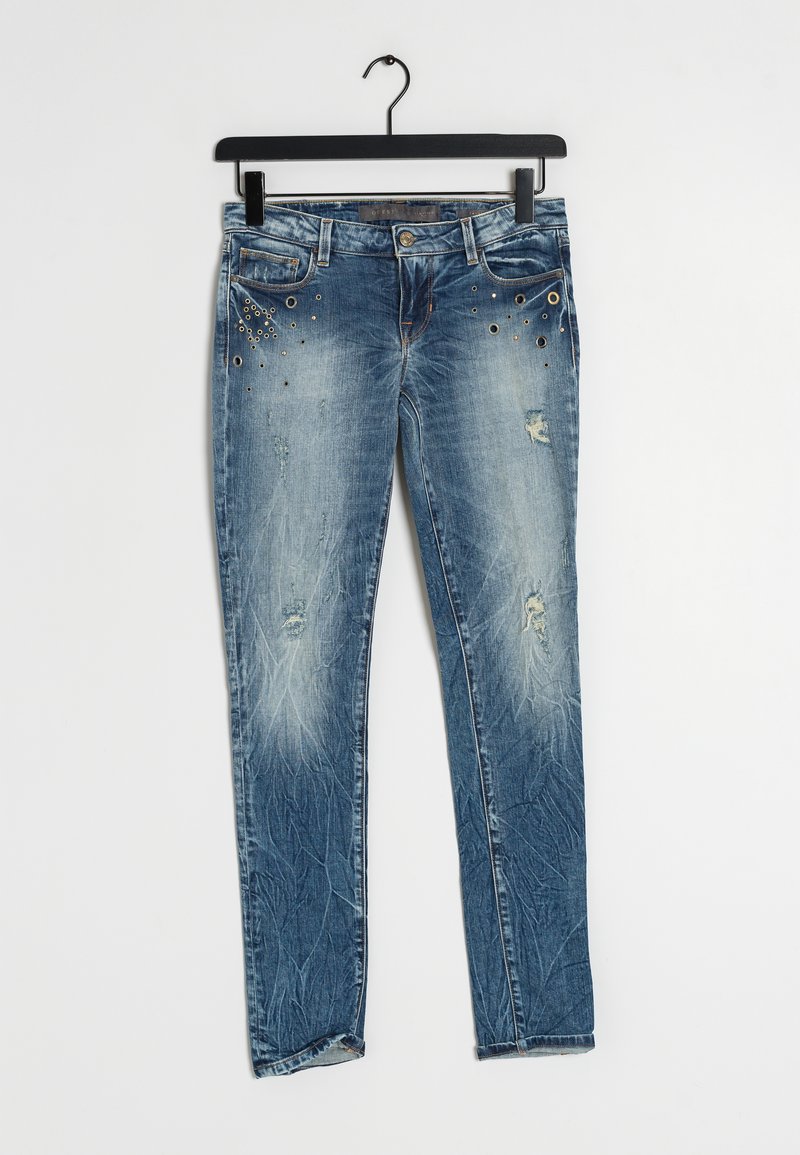 Ljusblå denimjeans med slim fit, med slitna områden och metalliska nitar nära fickorna. Hänger från en svart galge.