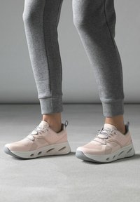 Scarpe da ginnastica rosa chiaro con una tomaia testurizzata e accenti grigi. Suola rotonda con aperture per traspirabilità e movimento flessibile.