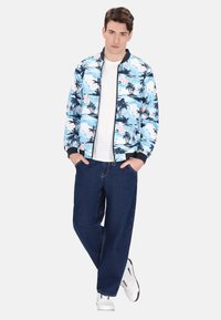 Jachetă bomber pentru bărbați, bleu deschis cu model de palmier, guler și manșete negre ribbate, asortată cu pantaloni de denim închisi și adidași albi.