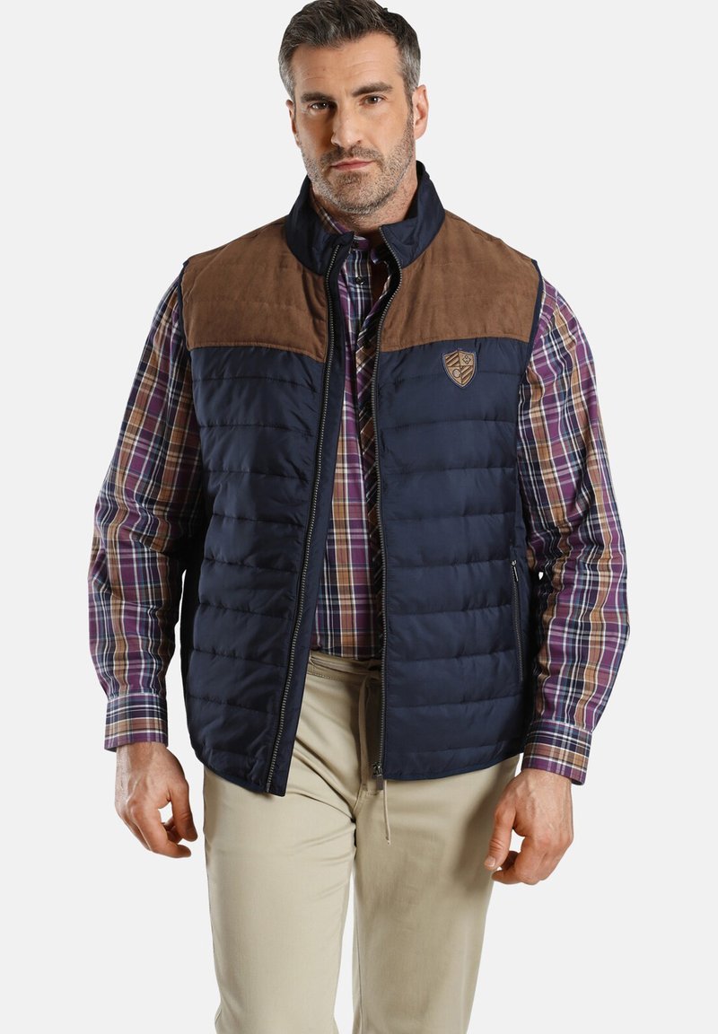 Navy Puffer-Weste mit braunen Wildleder-Schultern, Reißverschluss und Logo-Patch. Über einem karierten Hemd getragen, das eine strukturierte Gestaltung und Textur aufweist.