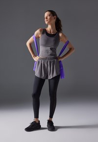 Idretts sett som inneholder en grå tanktop, grå shorts og svarte leggings. Lilla motstandsbånd liggende over armene. Svarte treningssko.