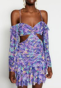 Lilla blomsterprintet kjole med ærmer uden skuldre, rynket tekstur, udskæringsdetaljer og flæset kant. Design i letvægtsstof.