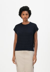 Navy gestrickter Pullover mit kurzen Ärmeln und geripptem Saum. Verfügt über ein strukturiertes Muster und einen runden Ausschnitt. Kombiniert mit einem beigen Rock.