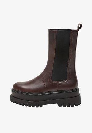 Bruine leren enkelboot met zwarte elastische zijpanelen, stevige zwarte zool en aantrekloop. Heeft een gladde textuur en een afgeronde neus.