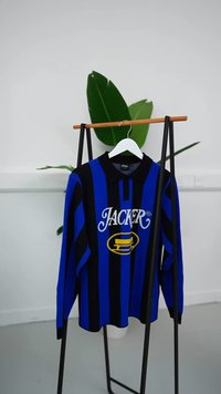 Blå og svart stripete langermet polo skjorte med "JACKER"-logo i hvitt og gult, med krage og ribbede mansjetter, hengende på en kleshenger.