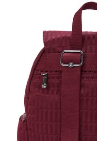 Zaino bordeaux con superficie texturizzata, dotato di cerniera argentata, tracolla regolabile e un accento metallico rettangolare nella parte superiore.
