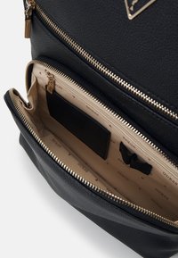 Borsa in finta pelle nera con texture, dotata di zip dorate e tasche interne. Foderata in beige con un motivo a logo ripetuto. Presenta un dettaglio a logo triangolare.