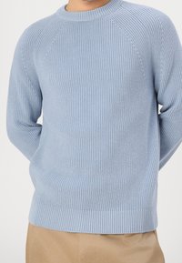Light blue knitted sweater with a ribbed texture, crew neckline, and raglan sleeves, paired with a beige trouser.