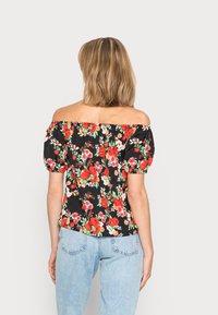 Haut noir floral à épaules dénudées avec manches bouffantes, orné de fleurs rouges et blanches, doté d'une coupe décontractée. Associé à un jean en denim bleu clair.