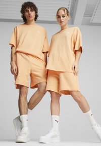 Ferskenfarvede bomulds-t-shirts og shorts med en afslappet pasform, parret med hvide platform sneakers og strømper med høj kant, der har sorte logoer.