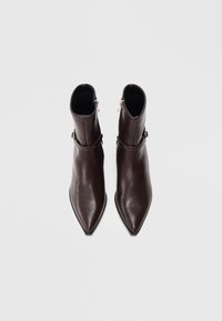 Hnědé kožené kotníkové boty s špičatou špičkou, s uzávěrem na zip a detailem pásku. Hladká textura a elegantní design.