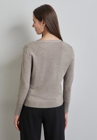 Beige tröja med rund halsringning, långa ärmar och ribbad fåll. Mjuk textur och figurnära silhuett, tillsammans med svarta byxor.