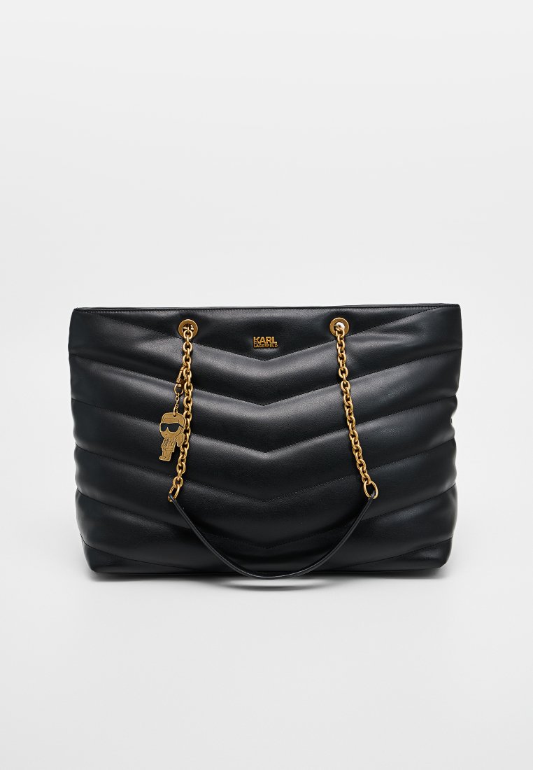 Bolso tote de cuero negro con un diseño acolchado en forma de chevron, correas de cadena dorada y un adorno decorativo. Presenta una textura suave y un logo.