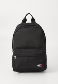 Sac à dos noir en tissu durable, doté d'une poche avant avec fermeture éclair, d'une poignée sur le dessus et d'un patch logo Tommy Jeans sur le bas à l'avant.