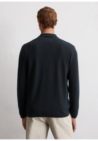 Dark navy long-sleeve polo sweater with a textured knit, ribbed collar, and a relaxed fit, worn over light-colored trousers.