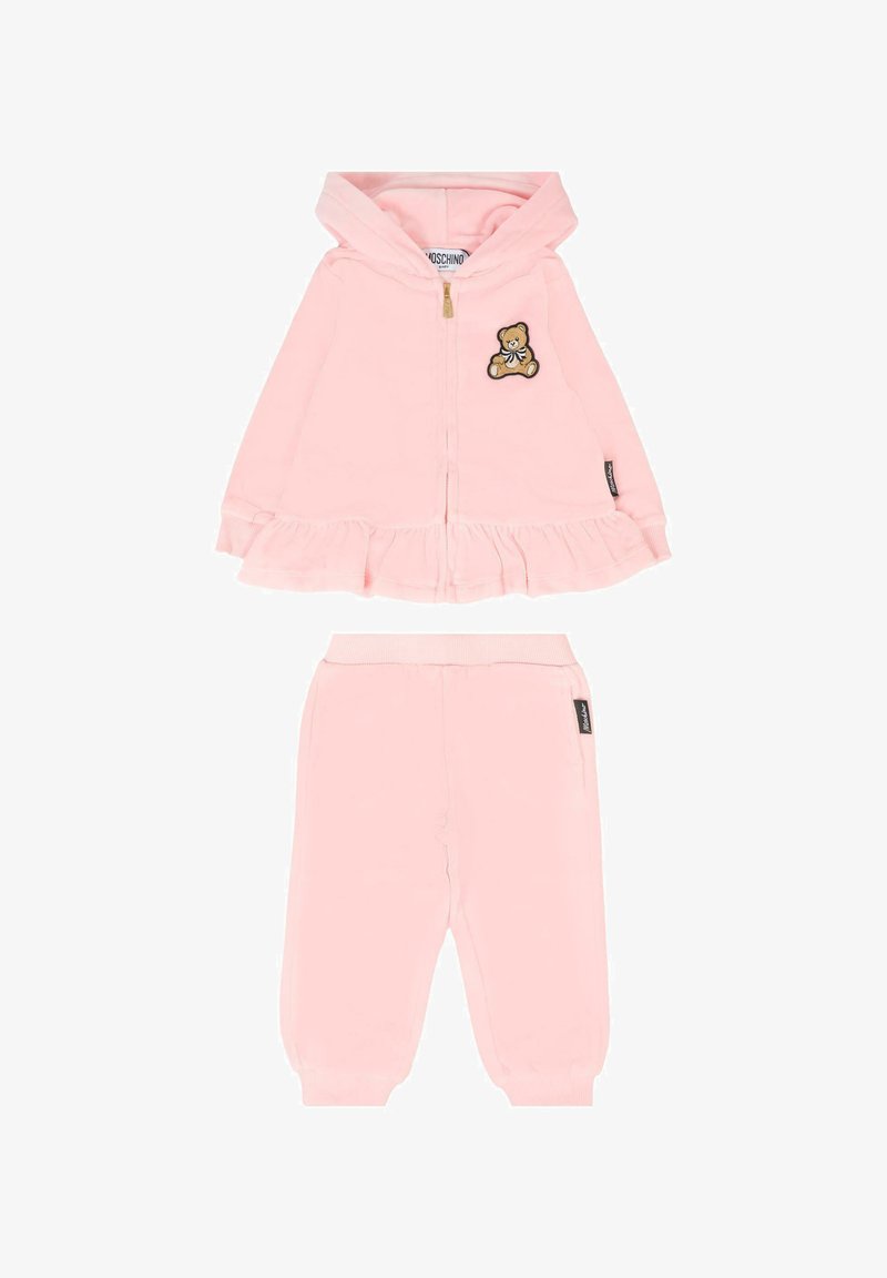 Różowy dres dziecięcy z kapturem zapinanym na zamek, ozdobiony naszywką w kształcie misia i falbaną na dolnej krawędzi, w zestawie z spodniami na elastycznej talii. Miękka tkanina.