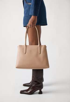 Lys beige læder tote taske med to lange håndtag, glat tekstur, minimalistisk design og subtilt prægede logo foran.