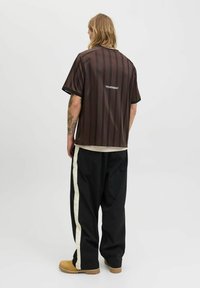 Brunstribet kortærmet skjorte med løs pasform, båret med sorte bukser med en creme farvet side-stribe og beige slip-on sko.