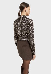 Langere mouwen shirt met zwart en crèmekleurig abstract patroon, gecombineerd met een mini-jurk van bruine corduroy met achterzakdetail.