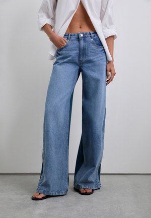 Lys blå denim brede ben jeans med høj talje, der har forlommer og knaplukning. Glat tekstur, afslappet pasform og fuld længde.