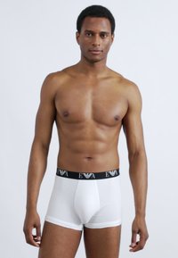 Άσπρα μπόξερ σλιπ με μαύρη ελαστική μέση που φέρει την ετικέτα "EVA." Το ύφασμα φαίνεται λείο και εφαρμοστό, δίνοντας λεπτομέρεια σε μια στενή σχεδίαση.
