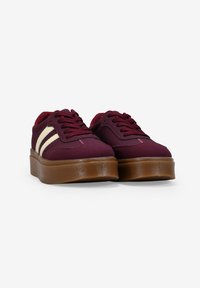 Zapatillas burdeos con rayas blancas, suela de goma, cuello acolchado y parte superior de tejido texturizado. Presenta cordones redondos y una silueta robusta.