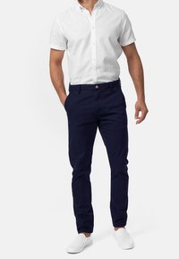 White short-sleeve button-up shirt paired with navy blue chinos and white slip-on shoes. The outfit features a classic fit with a clean design.