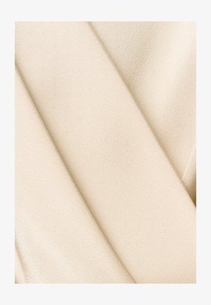 Tissu satin beige lisse plié en diagonale, montrant une texture douce et un léger éclat sous la lumière.
