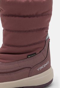 Lila vízálló csizma quiltált, párnázott felsőrésszel. Jellemzője a texturált alsó szakasz és a fekete-arany GORE-TEX címke. Fehér "VIKING" márkajelzés.