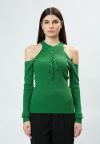 Grüner gerippter Pullover mit Halterneck-Design, Kalt-Schulter-Ausschnitten und einem vorderen Schnürdetail. Lange Ärmel mit eng anliegenden Bündchen.