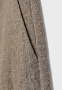 Beige tekstureret linnedstof med en synlig søm og et foldet hjørne mod en lys baggrund.