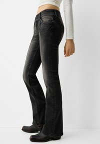 Jeans flare in denim nero con chiusura a due bottoni e leggeri dettagli sbiaditi. Texture liscia; indossati con zoccoli neri per creare contrasto.