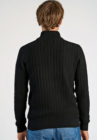 Schwarzer Strickpullover mit hohem Kragen, strukturiertem Rippenmuster und enganliegendem Bündchen sowie Saum. Einfaches Design, geeignet für die Freizeit.