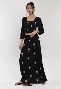 Svart tvådelad outfit bestående av en kortärmad topp med puffärmar och en lång kjol, båda med vit palmer broderi.