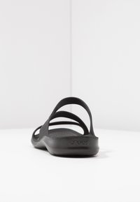 Black rubber sandals with three adjustable straps, textured footbed, and flat sole. Features a logo on the heel. Minimalist design.
