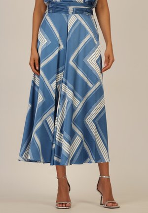 Frau trägt einen blauen Rock mit weißen, geometrisch schrägen Streifen, kombiniert mit silbernen High-Heel-Sandaletten mit Knöchelriemen.