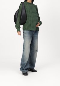 Haut long à manches longues texturé vert, jeans bleu délavé amples avec un genou déchiré, sac à main en cuir noir et chaussures noires.